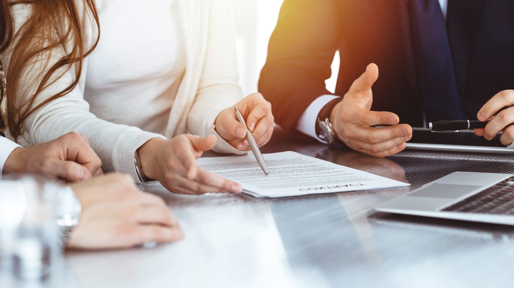 Business people discussing contract while working together in sunny modern office. Unknown businessman and woman with colleagues or lawyers at meeting