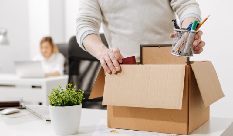 Upset office manager packing the box and leaving the office making someone redundant
