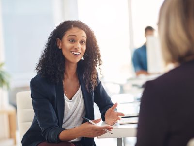 Interview with a happy, excited and confident human resources manager talking to a shortlist candidate for a job. Young business woman meeting with a colleague or coworker in her office at work.