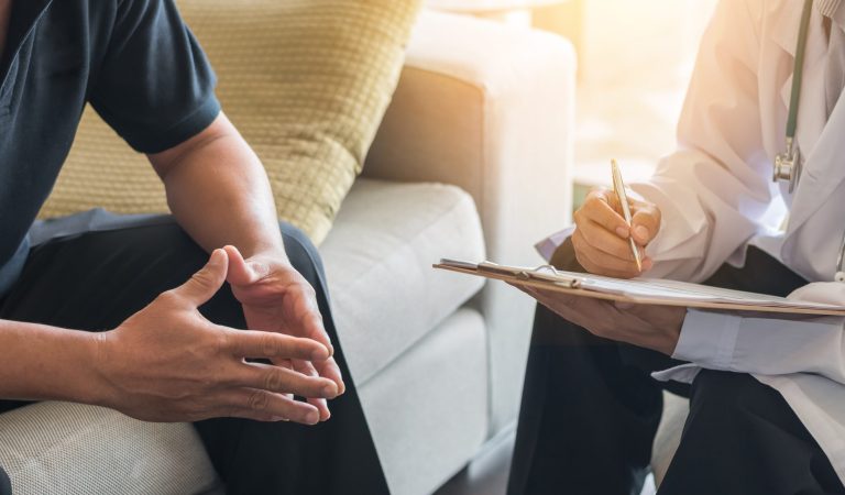 Doctor consulting male patient, working on diagnostic examination on men's health disease or mental illness, while writing on prescription record information document in clinic or hospital office